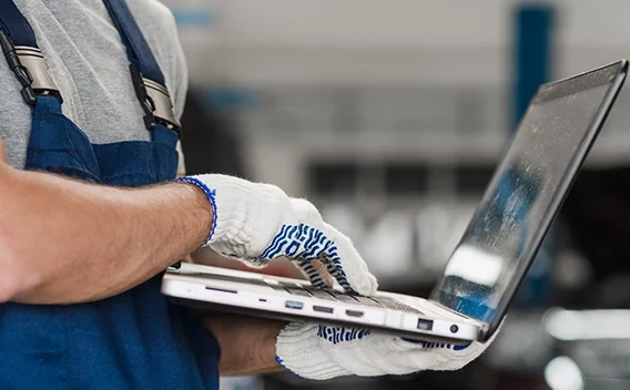 Man with work bibs and gloves holding a laptop
